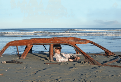 Auto am Strand im Sand versunken, Mann sitzt im Sand im Auto