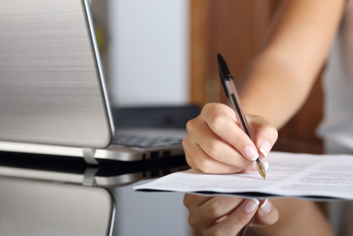 Frau schreibt handschriftlich etwas auf ein Blatt Papier